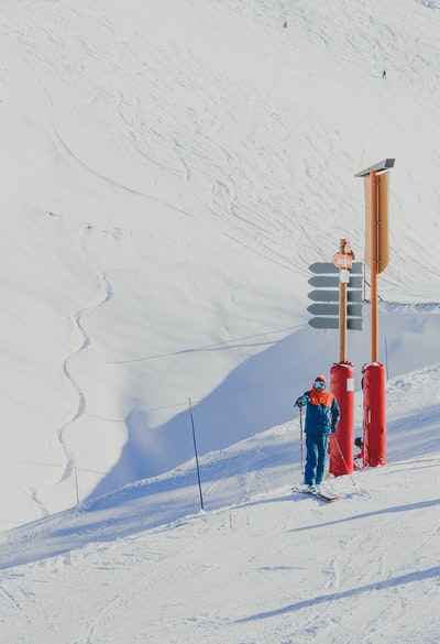 身穿蓝色夹克的男子手持滑雪杆站在红棕色柱子附近